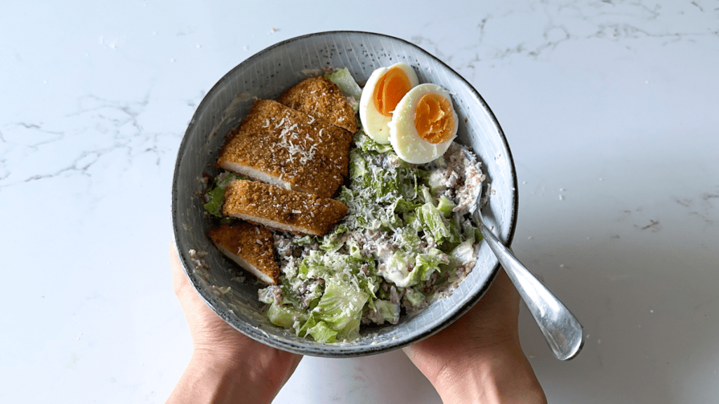 A hand-held bowl of a chicken salad featuring the 4-grain rice blend mixed with lettuce, topped with breaded chicken and boiled egg.
