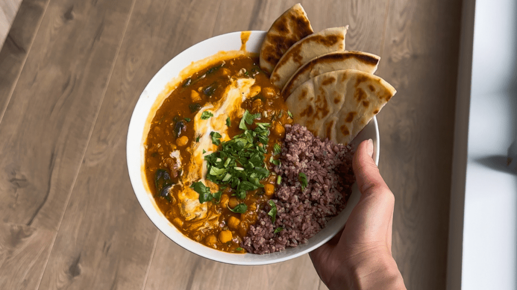 A hearty bowl of vegetable curry served with a side of purple 4-grain rice blend and toasted naan bread.