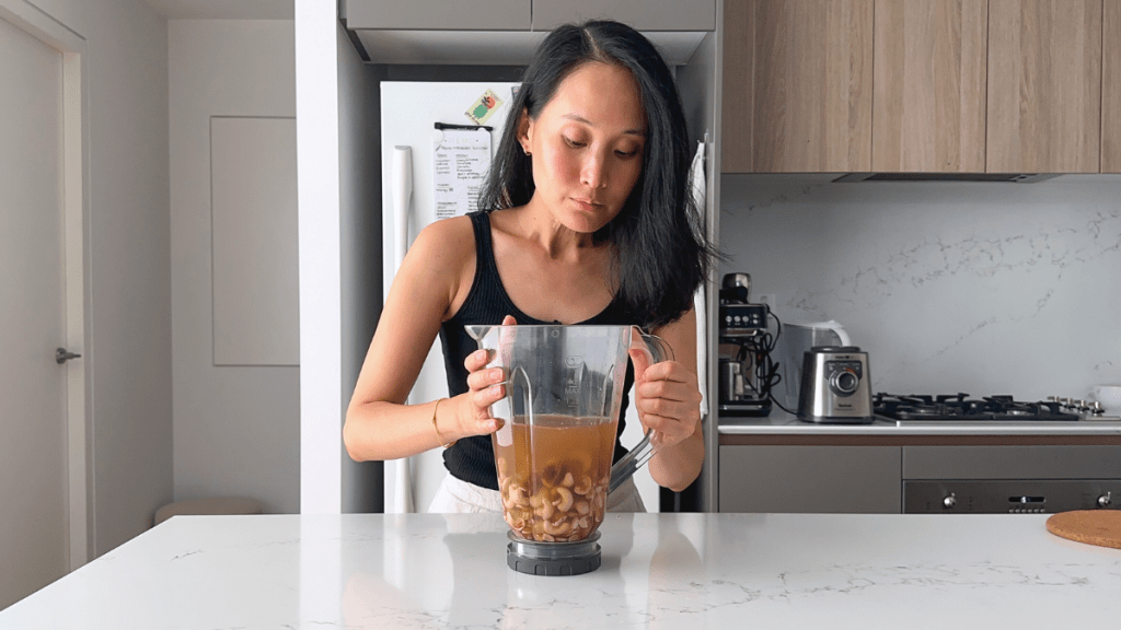 Raw cashews and pitted dates soaking in water inside a blender jug.
