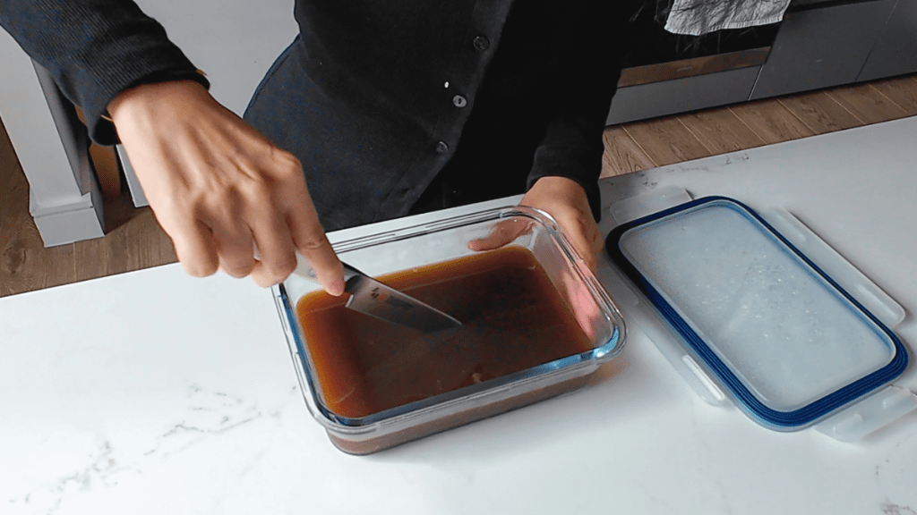 A person using a sharp knife to cut a tray of dark, set coffee jelly into a grid of small cubes.