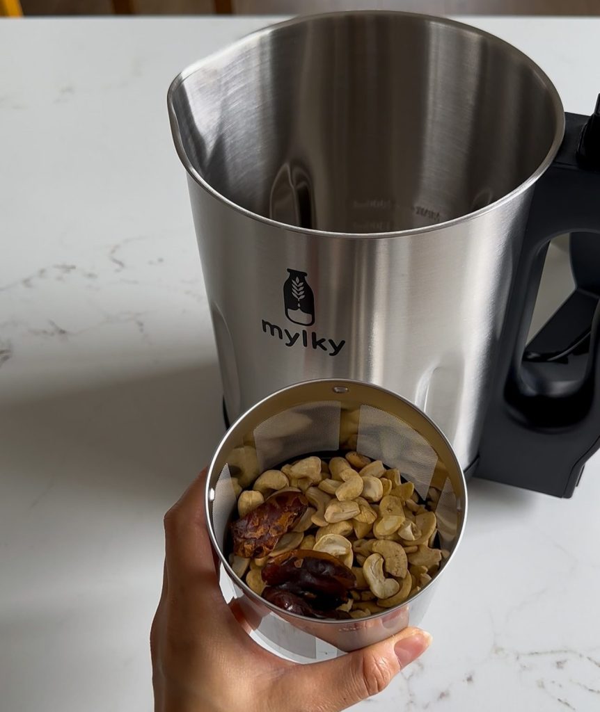 A close up view of raw cashews and dates inside the stainless steel filter basket of the Mylky machine.