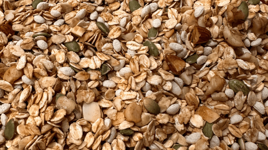Close up texture shot of toasted rolled oats, cinnamon, pepitas, pecans, walnuts, and almond flakes.